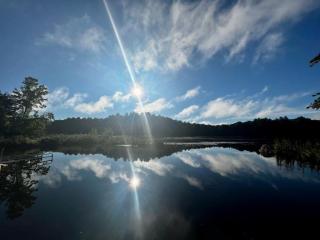 A late afternoon sun, just above the crest of a hill, is reflected in the water of a pond.